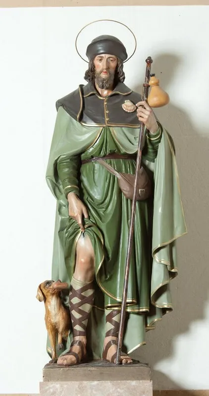 Imagem de São Roque em escultura policromada: homem barbado de chapéu e auréola, manto verde, cajado com cabaça, mostrando a ferida na perna, com um cão aos seus pés