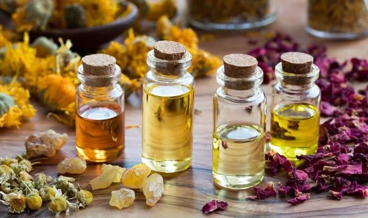 Frascos de vidro com rolha contendo óleos essenciais, cercados de flores secas de calêndula, camomila, pétalas de rosa e resina