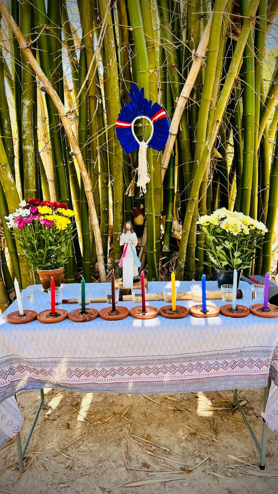 O Congá erguido sob o bambuzal: mesa com toalha branca, velas coloridas em pratos de barro, copos d'água, dois vasos de flores, a imagem de Jesus e, acima, um cocar azul preso aos bambus.